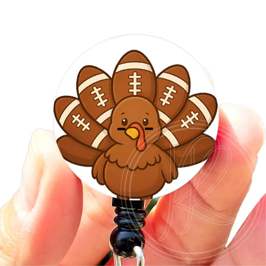 A person's hand holding a round badge featuring a cartoon turkey with footballs on its back.